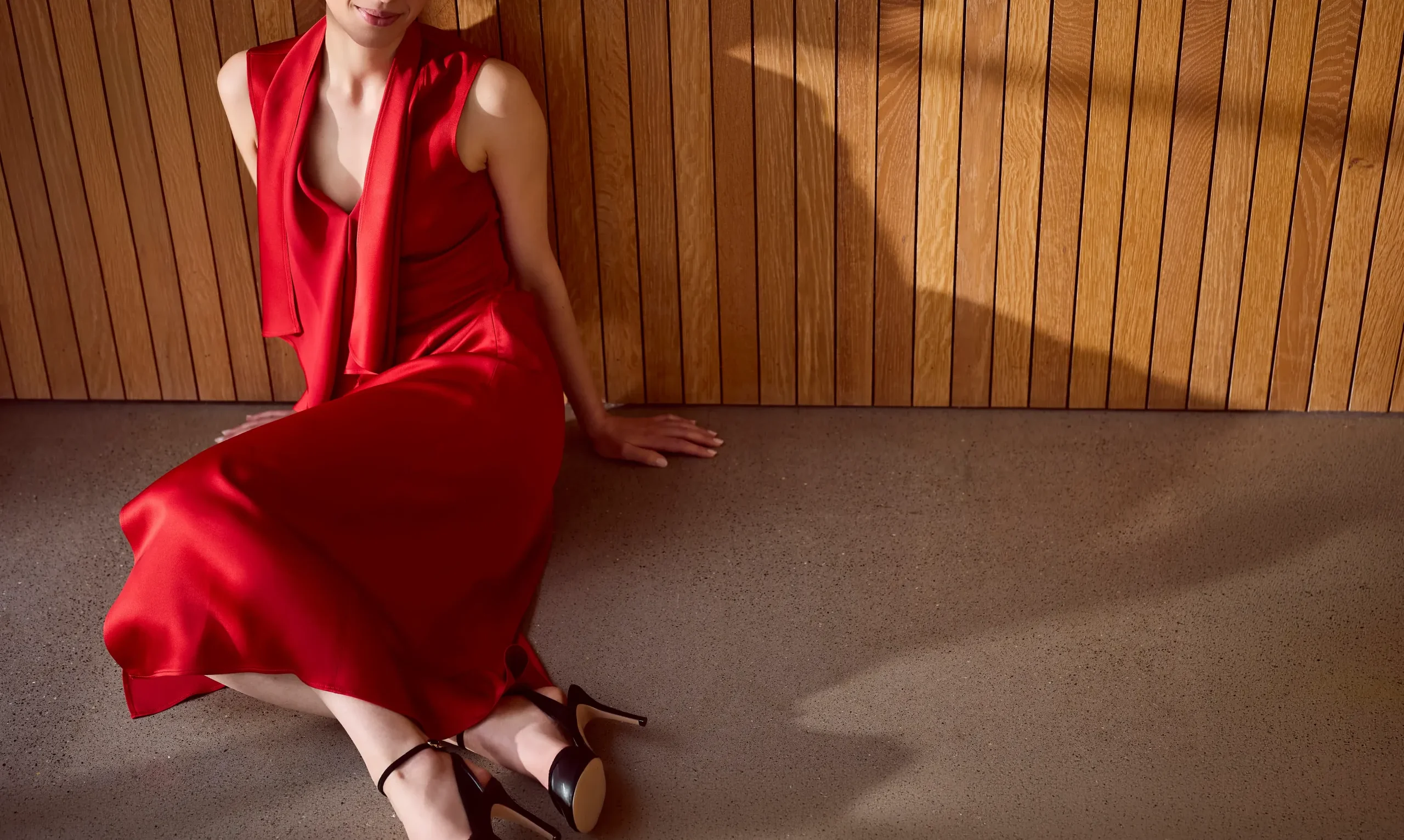 Sarah, high-class independent escort in London, in a red silk dress against a wooden wall