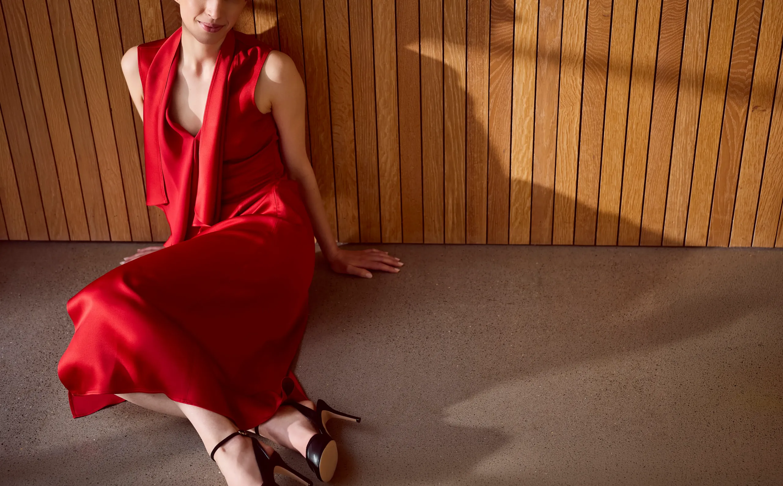 Sarah, high-class independent escort in London, in a red silk dress against a wooden wall